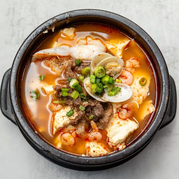 Naju Tofu's Korean soft tofu stew with beef, shrimp, clams, and green onions in a black bowl.