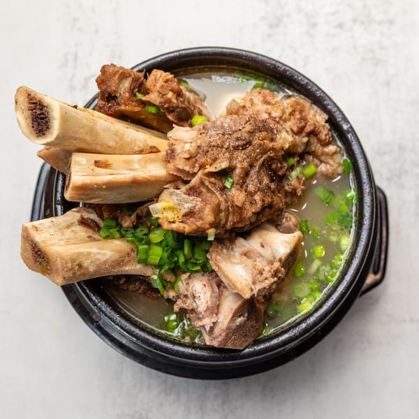 A black bowl of Naju Tofu's Korean beef short rib soup with green onions.