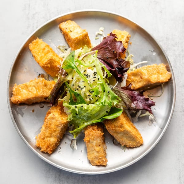 Golden-fried tofu pieces arranged in a circle around a fresh green and red lettuce salad on a metal plate.