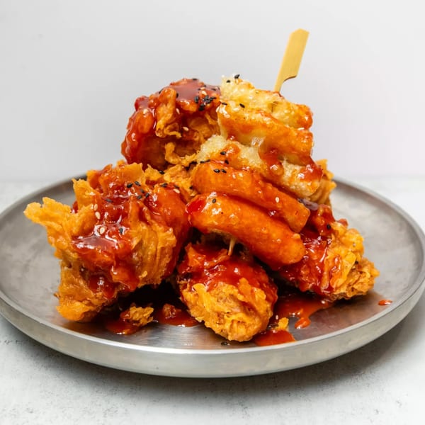 Korean fried chicken and tteokbokki skewers, drizzled with red sauce and sesame seeds on a metal plate.