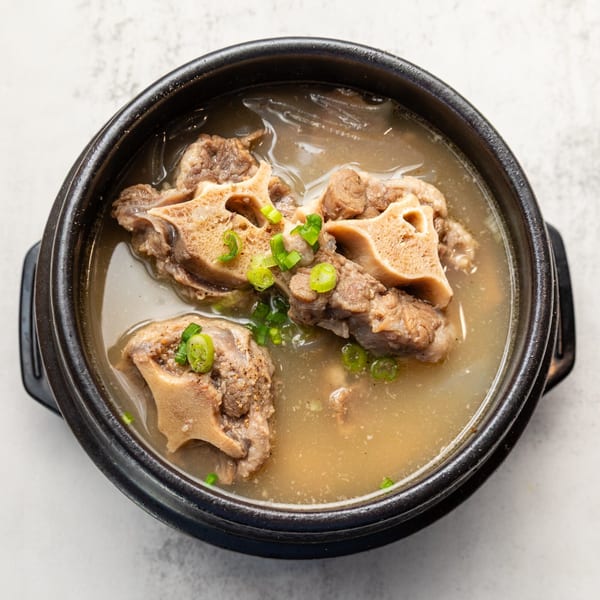 Naju Tofu's Korean oxtail soup, garnished with green onions, in a black stone bowl.