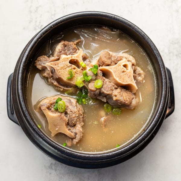 A black bowl of Naju Tofu's Korean oxtail soup, garnished with green onions.