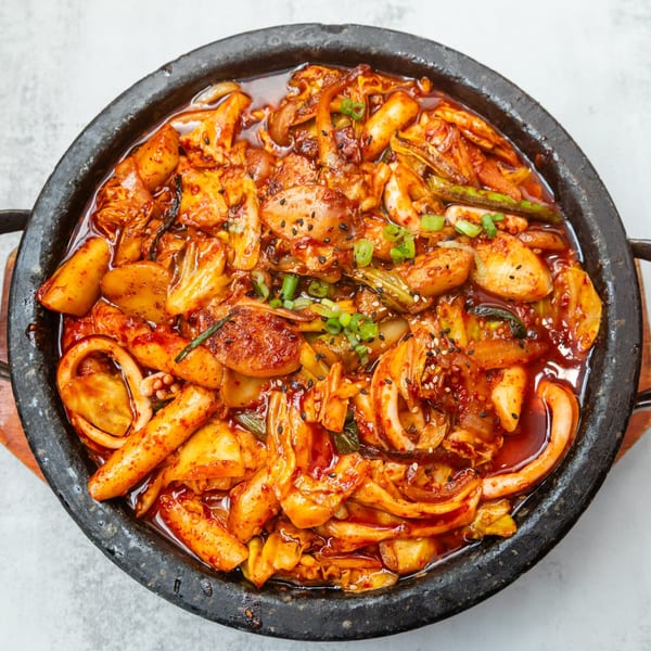 Spicy Korean stir-fried squid and rice cakes with vegetables in a black stone pot.