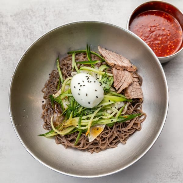 Korean cold buckwheat noodles with beef, cucumber, radish, and a boiled egg, served with spicy sauce.